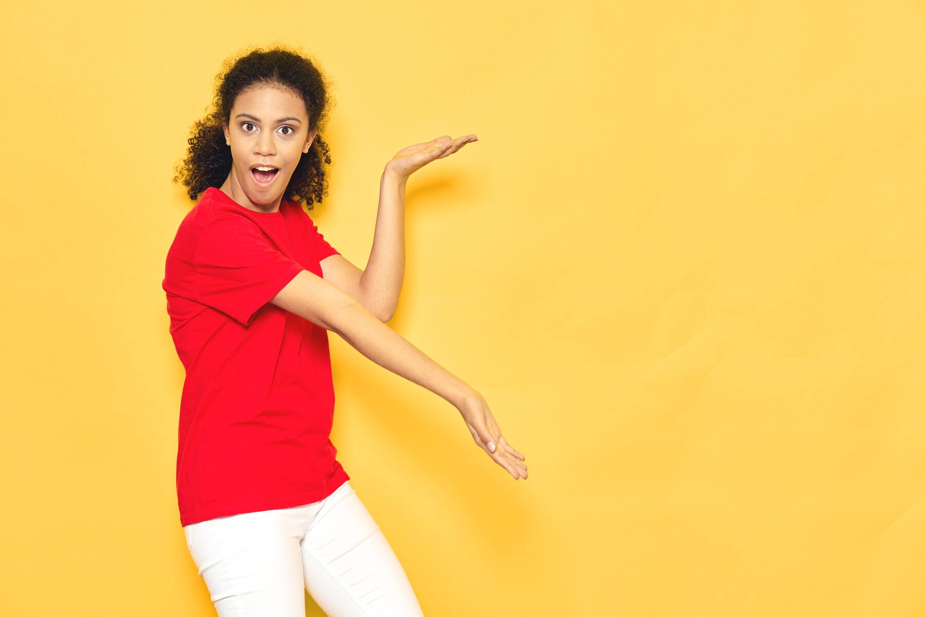 Pretty Woman with Curly Hair in a Red T-Shirt on a Yellow Background Gesture with Her Hands