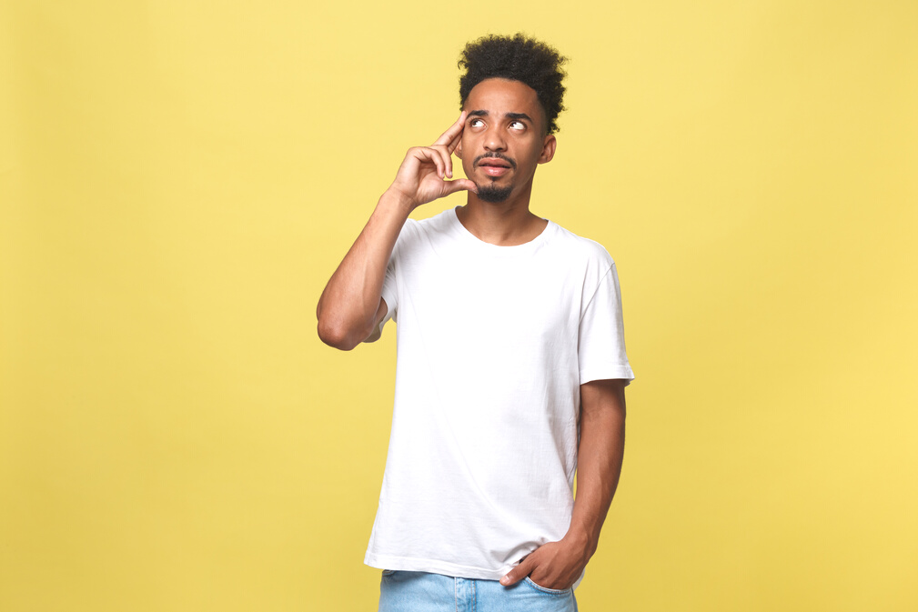 Image of Thoughtful Young African Man Dressed in White Tshirt Standing Isolated over Yellow Background.